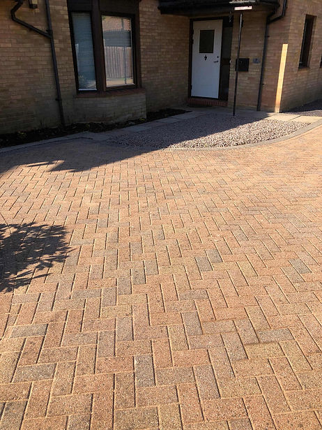 Curved brick paved driveway bordered by decorative gravel beds next to a modern property