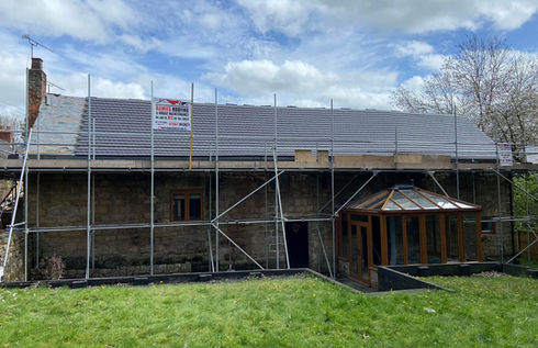 A stone building with scaffolding and a partially completed roof under a cloudy sky