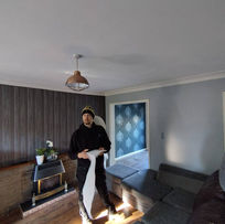 A person stands in a cozy living room holding a piece of white paper