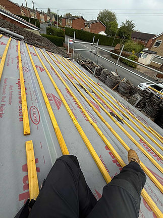 View from a rooftop showing yellow wooden beams laid out on underlayment material with branding