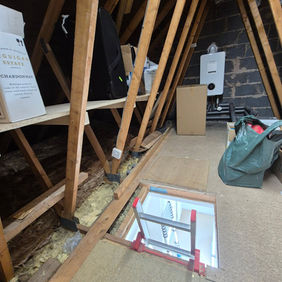 Spacious attic conversion in progress with exposed timber trusses and flooring tools