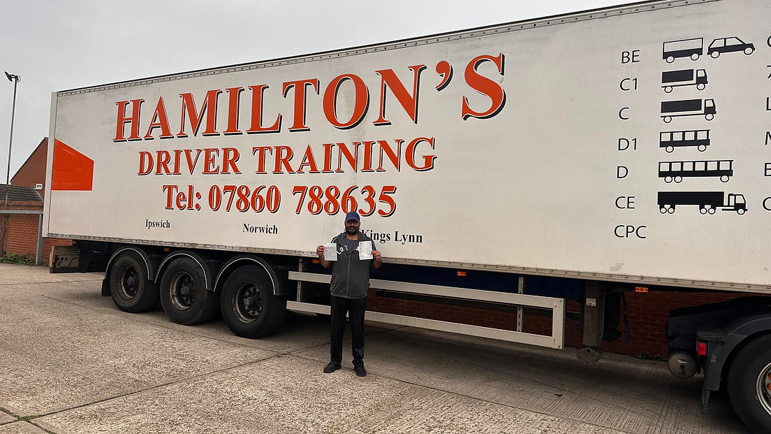 Man holding certificates stands in front of a large truck with "Hamilton's Driver Training" on its side