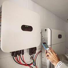 A person uses a smartphone to monitor a solar inverter and battery system mounted on a white wall