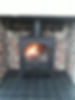 A black wood-burning stove with a glass door shows a warm, glowing fire