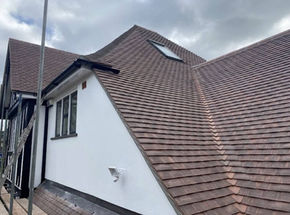 Modern house with steep brown tiled roof, skylight, and white walls with dark window frames