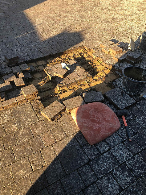 An ongoing driveway repair showing black sand beds, loose blocks, a mallet, and a bucket