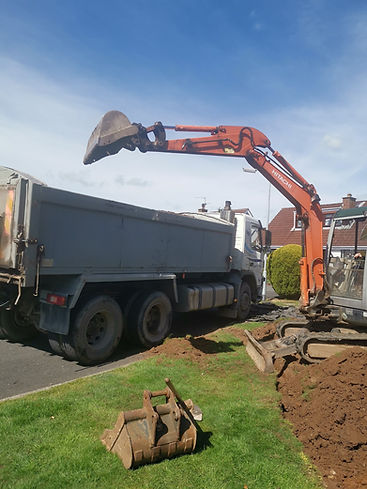 Orange excavator loads soil into gray dump truck on residential street