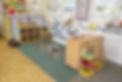 Bright classroom with colorful toys on shelves, a cozy play mat, and decorative wall displays
