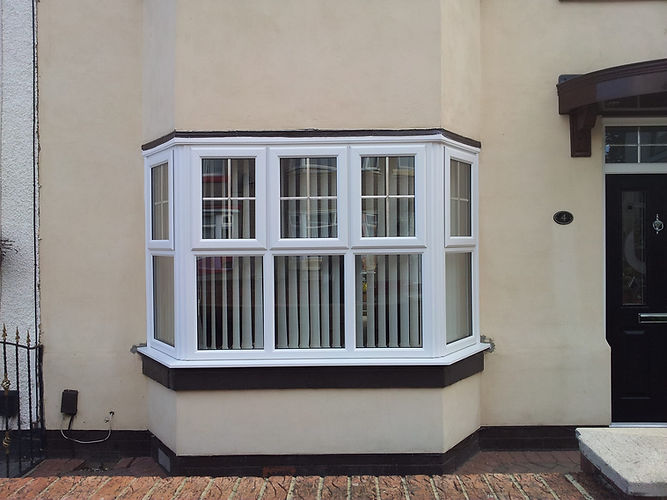 White bay window with vertical blinds on a beige house exterior