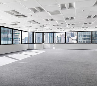 Bright, empty office space with gray carpet, large windows showing a cityscape