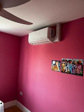 Wall-mounted air conditioner and ceiling fan in a pink-walled room with a white ceiling