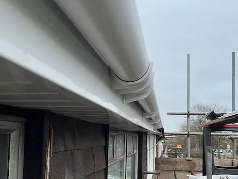 A newly installed white gutter system is shown on a rooftop under overcast skies
