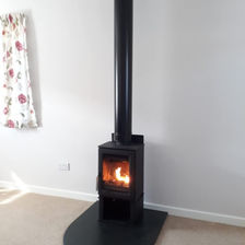 A small black wood-burning stove with a roaring fire, set against a white wall