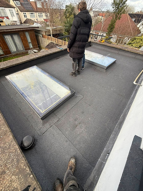 A man stands on a rooftop beside a skylight, overlooking the surroundings from an elevated position