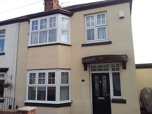 Beige two-story house with white-framed windows, a black door under a small awning