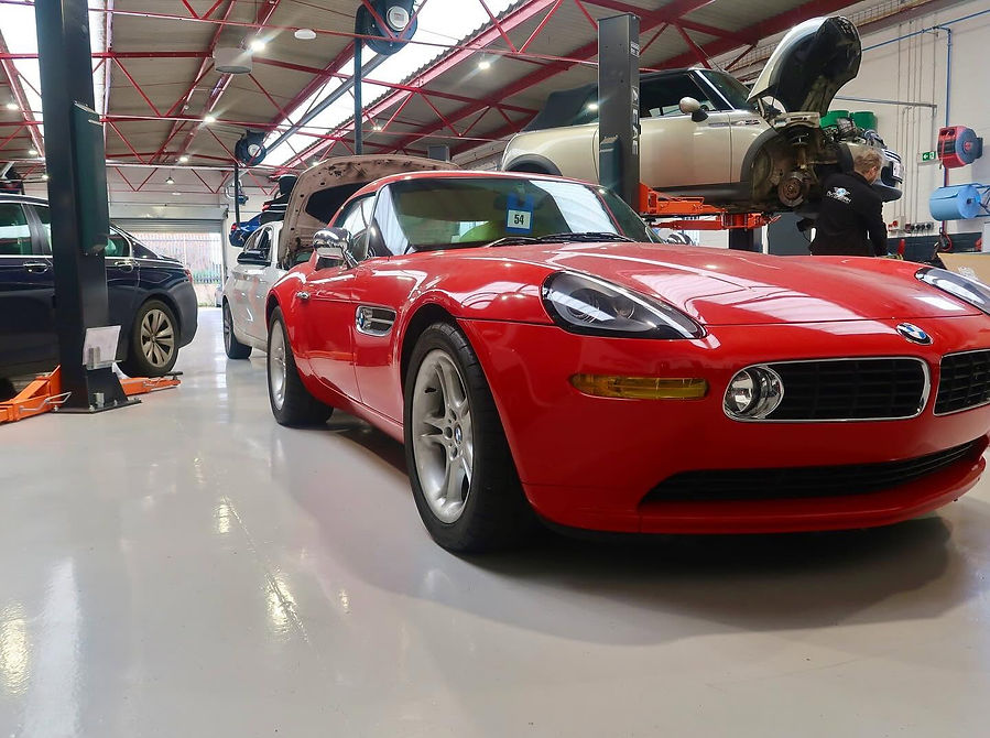 Front view of a bright red sports car parked in a line with other vehicles inside a workshop bay