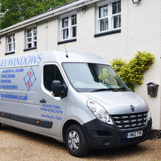 A silver van branded "Ashley Windows" is parked outside a two-story building