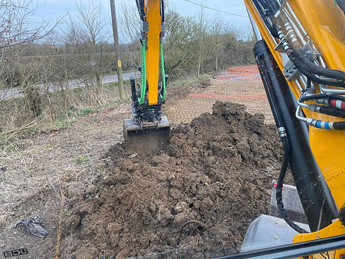 Tracked yellow excavator digging a trench in muddy ground on a construction site