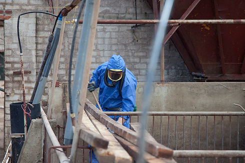 Worker in a blue hazard suit handling building materials on an outdoor industrial or construction site