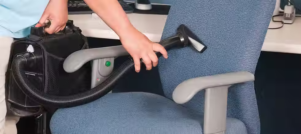Close-up of a cleaner using a vacuum attachment to sanitise a blue office chair
