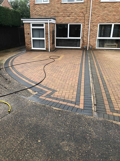 Curved black and grey block paved driveway with pressure washing hose laid across the surface