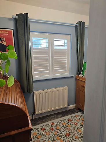 High quality white plantation shutters installed in a residential room window next to a radiator