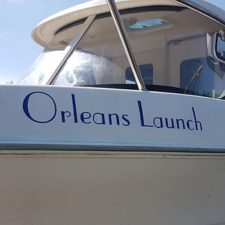 The side of a white boat with "Orleans Launch" in blue letters, against a sunny sky