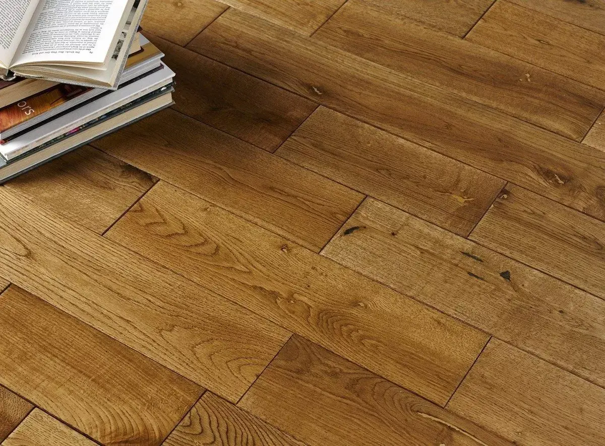 Stack of books on warm, honey-colored wooden floorboards with intricate grain patterns