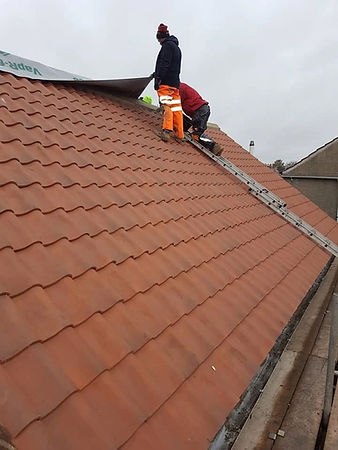 Roofer actively installing roof tiles on a steep pitched roof slope