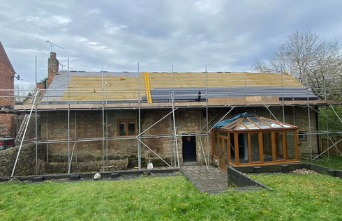 A house under construction with scaffolding along its stone facade and a new roof being installed