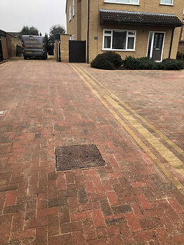 Close-up of weathered red and brown block paving stones around a utility manhole cover