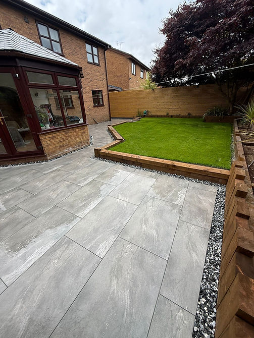 Landscaped backyard patio with grey tiles and green lawn