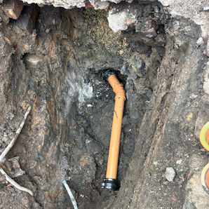 New orange plastic drainage pipe installed deep inside an excavated earth trench