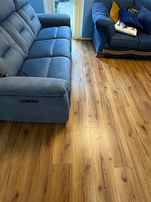 Warm, medium-toned wood plank flooring next to a blue upholstered sofa in a living room