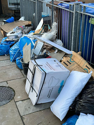 Pile of discarded items on a sidewalk, including blue bags, cardboard boxes