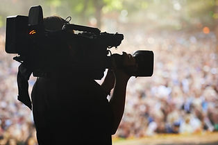 A silhouette of a cameraman filming an outdoor event with a large camera