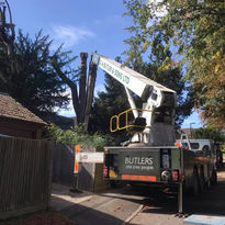 A crane truck is parked on a sunny street near trees, with "BUTLERS" visible on the side