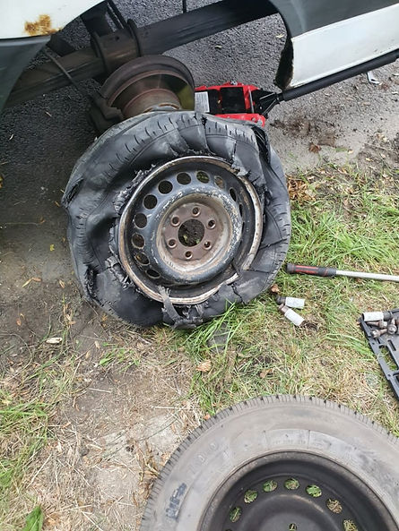 Severely damaged car tire with torn rubber lies on grass nearby tools