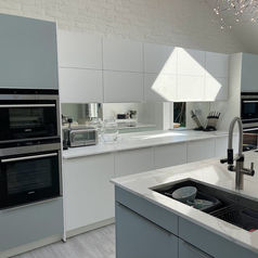 An open-plan dining and living area looking into the modern sage green kitchen, with contemporary gray chairs around a white dining table in the foreground