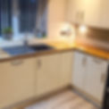 Kitchen sink and wooden countertop set against white tiled walls with warm under-cabinet lighting