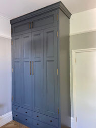 Tall blue wardrobe with paneled doors and brass handles, flanked by white walls