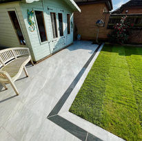 A sunny backyard with a green lawn bordered by stone tiles