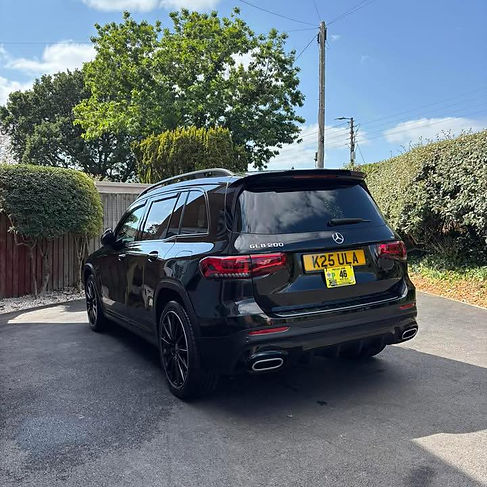 A sleek black SUV is parked on a driveway, surrounded by greenery and a wooden fence