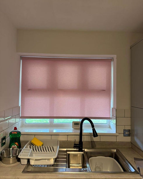Pink roller blind pulled down over a window above a kitchen sink and black faucet