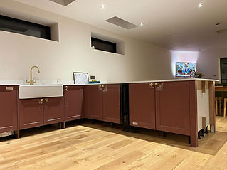 Low-angle shot of light oak flooring in a kitchen featuring dusty-pink base cabinets and a white farmhouse sink