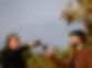 Two men clink wine glasses outdoors against a backdrop of blurred autumnal vines