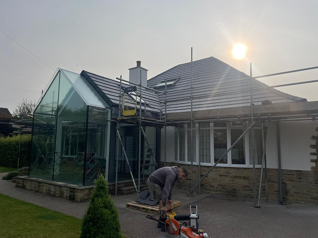 A house under renovation with scaffolding around its roof, a glass extension visible