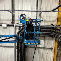 Worker in a blue cherry picker lift installing overhead electrical conduit