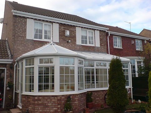 Two-story brick house with a white conservatory featuring large windows and a pitched glass roof