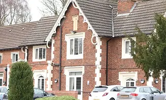 Two-story brick house with white trim, gabled roof, leaded windows, and cars